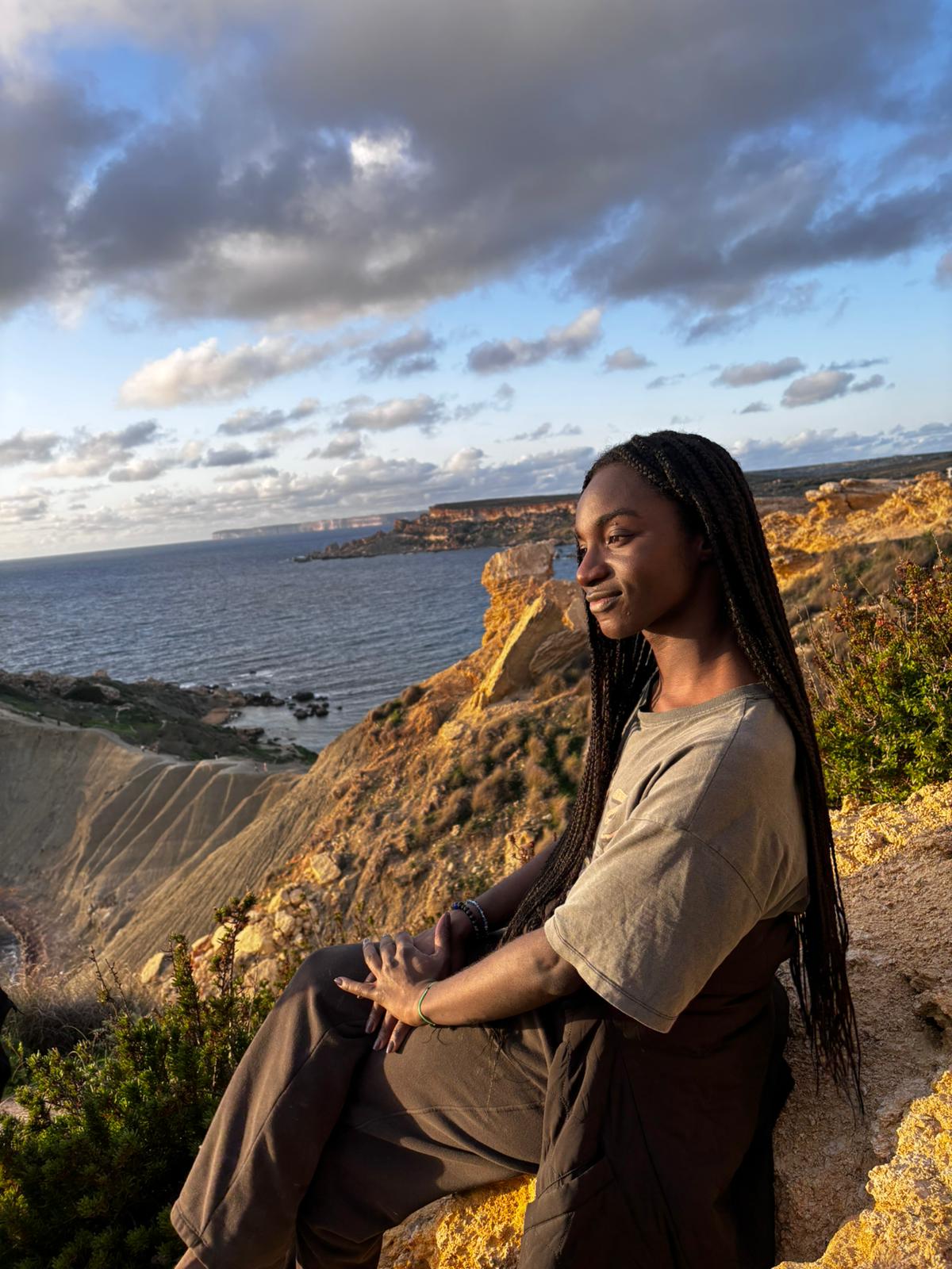 Jennifer assise sur une falaise à Malte, face à la mer
